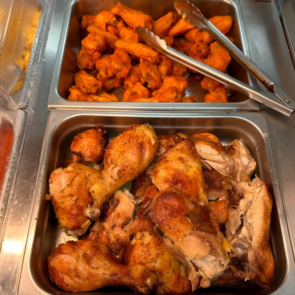 Two metal trays of food, one with golden-brown roasted chicken pieces and another with orange chicken wings.