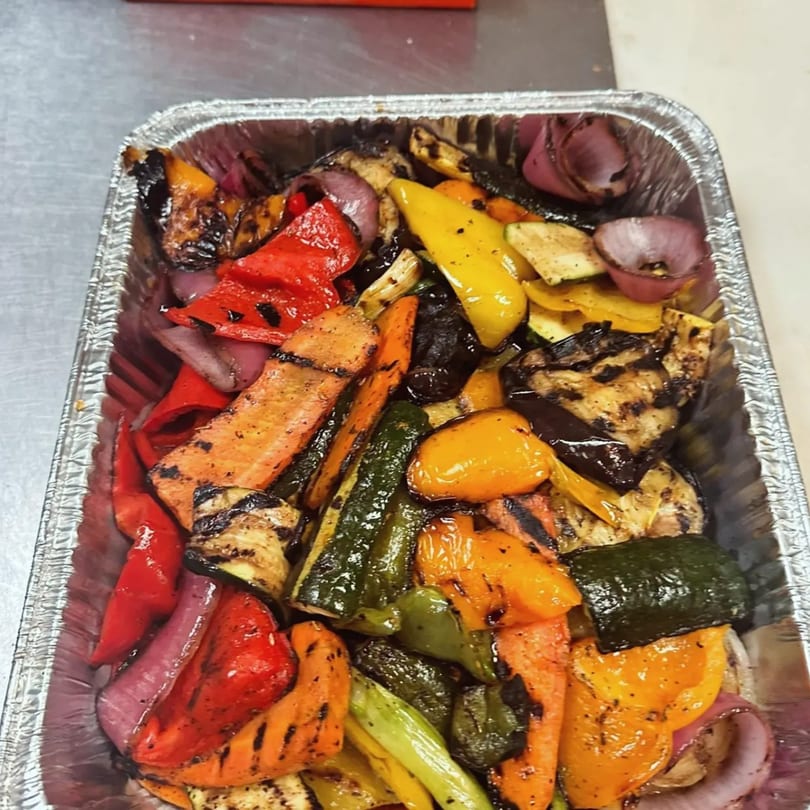 A foil tray filled with colorful grilled vegetables, including bell peppers, zucchini, carrots, and red onions.