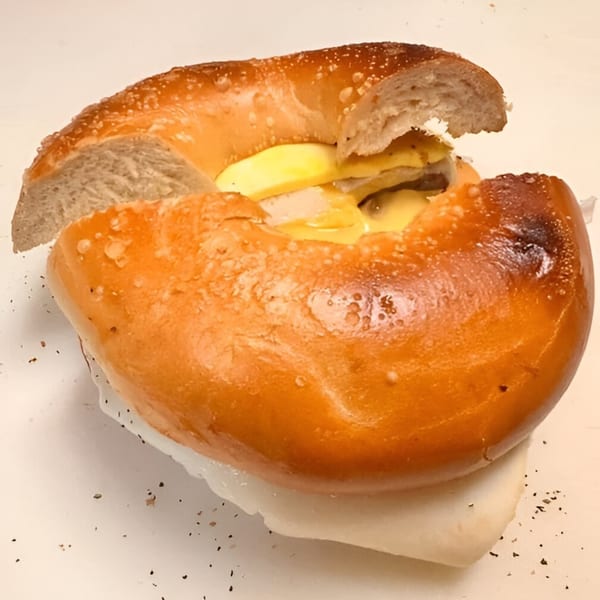 A close-up of a bagel sandwich filled with melted cheese and meat, on a white surface.