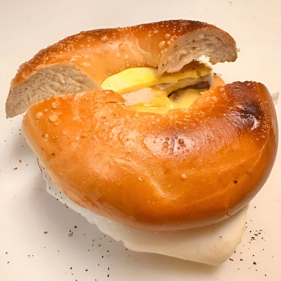 A close-up of a bagel sandwich filled with melted cheese and meat, on a white surface.