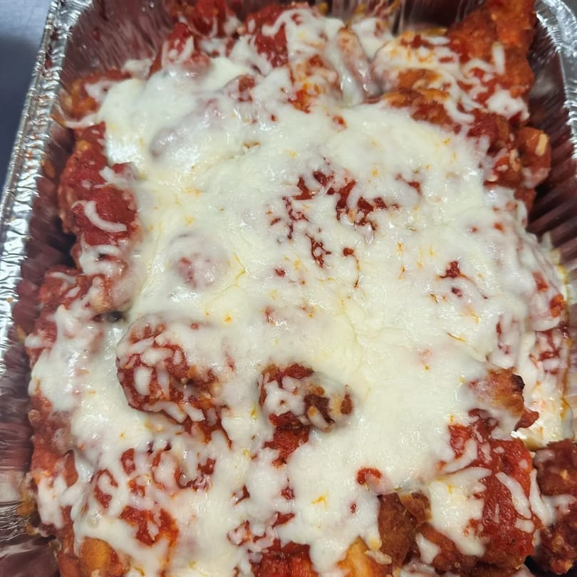 Close-up of baked ziti or chicken parmesan with melted mozzarella cheese and red sauce in a foil pan.